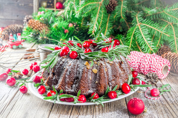 Homemade Christmas baking. Dark chocolate gingerbread christmas bundt cake with powdered sugar, fresh cranberries and rosemary, with xmas tree decoration