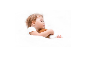 Little baby kid sleeps on a clean bedspread hugging a teddy bear. Caucasian child girl boy sitting dreams on big bed, white background