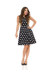 Beautiful Young Woman In Black Cocktail Dress In Polka Dots And High Heels Is Pointing Down And Talking