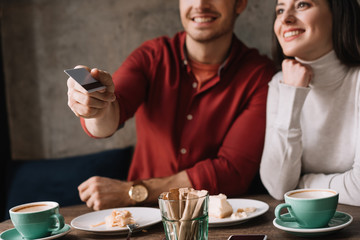 cropped view of young couple sitting in coffee shop while man holding credit card