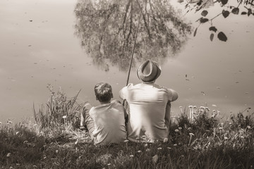 Back view of happy family on summer vacations concept. Father and son fishing together at river...