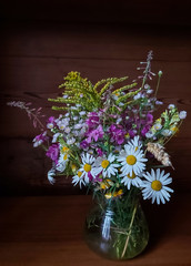 beautiful bouquet of bright wild flowers on a wooden background in a glass vase