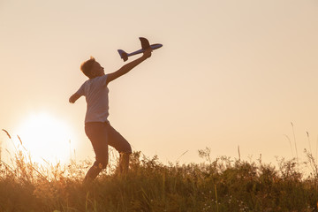 Black silhouette of cute happy cheerful child running fastly along grassy hill at countryside holding big toy plane in hand. Boy playing during sunset time in evening. Horizontal color photography.