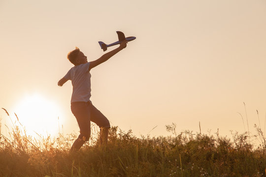 Black silhouette of cute happy cheerful child running fastly along grassy hill at countryside holding big toy plane in hand. Boy playing during sunset time in evening. Horizontal color photography.