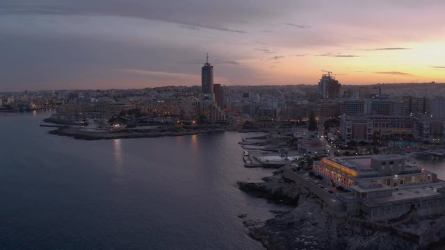 High Aerial shot orbiting around the coast of St Julians Malta. Baech at the sunset