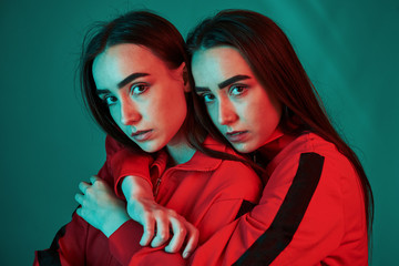 Calm and quiet. Studio shot indoors with neon light. Photo of two beautiful twins