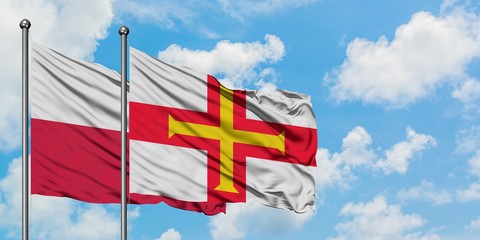 Poland and Guernsey flag waving in the wind against white cloudy blue sky together. Diplomacy concept, international relations.