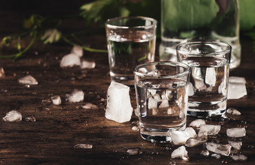 Cold vodka in shot glass, old wooden table, selective focus