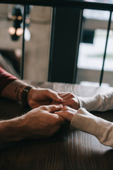 cropped view of couple holding hands on balcony in coffee shop