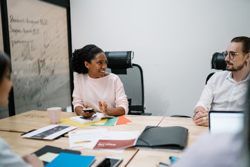 Happy team of professionals discussing ideas and effective solutions for improving work process at meeting table during brainstorming in modern office, employees collaborating on business project