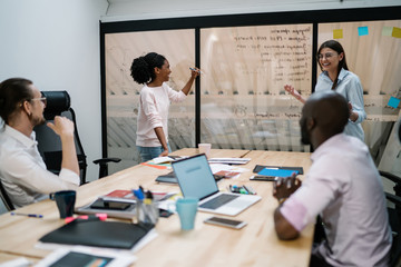 Cheerful male and female finance experts planning corporate project during brainstorming and briefing in conference room, happy smiling entrepreneurs talking about strategy in modern workshop