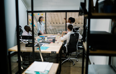 Multicultural employees collaborating on creating presentation writing ideas on office window during productive job, professional partners discussing information for business project on conference