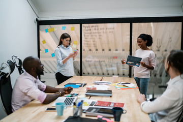 Multicultural group of creative people dressed in formal wear discussing business startup project at meeting table during brainstorming in modern office, collaborative process of financial experts