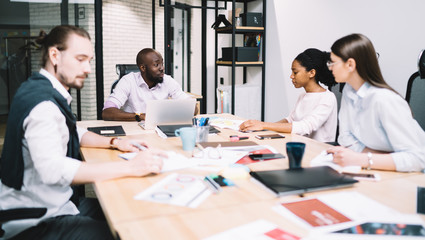 Multicultural team of male and female professionals dressed in formal wear discussing strategy and solution during working process and briefing in modern office, diverse experienced business people