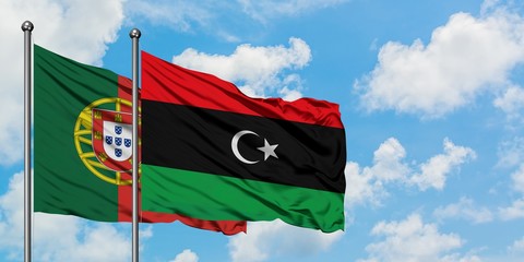 Portugal and Libya flag waving in the wind against white cloudy blue sky together. Diplomacy...