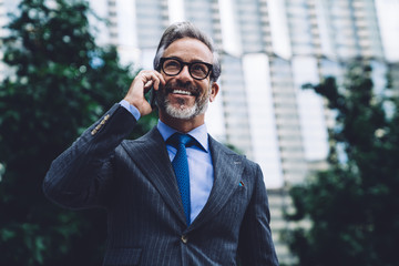 Happy mature businessman calling by smartphone at street