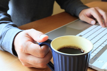 マグカップのコーヒーを飲みながらノートパソコンで仕事をする