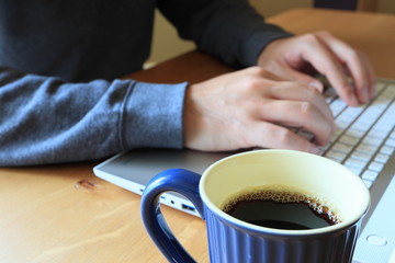 Fototapeta na wymiar マグカップのコーヒーを飲みながらノートパソコンで仕事をする