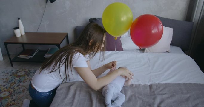 Caucasian mother brings balloon to her newborn baby laying on bed. RAW Graded footage 4K slow motion 50fps 