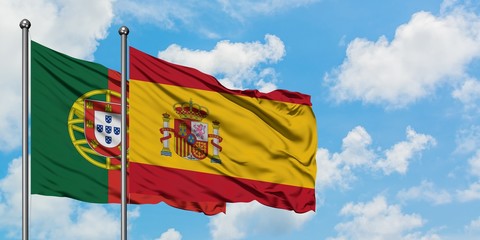 Portugal and Spain flag waving in the wind against white cloudy blue sky together. Diplomacy...