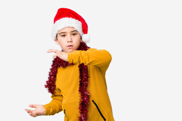 Little boy celebrating christmas day wearing a santa hat isolated shocked and amazed holding a copy space between hands.