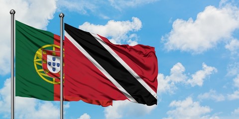 Portugal and Trinidad And Tobago flag waving in the wind against white cloudy blue sky together....