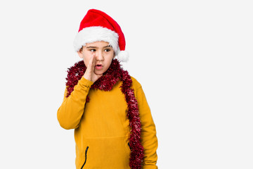 Little boy celebrating christmas day wearing a santa hat isolated is saying a secret hot braking news and looking aside