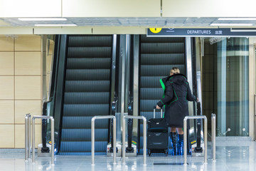 The alone woman on the escalator or moving staircase with inscription departure in English and Chinese in the international airport or railway station from the back moving upstairs with luggage