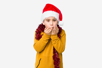 Little boy celebrating christmas day wearing a santa hat isolated folding lips and holding palms to send air kiss.