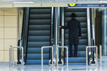 The alone man on the escalator or moving staircase with inscription departure in English and Chinese in the international airport or railway station from the back moving upstairs with luggage