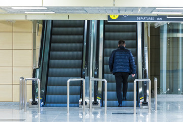 The alone man on the escalator or moving staircase with inscription departure in English and Chinese in the international airport or railway station from the back moving upstairs with luggage