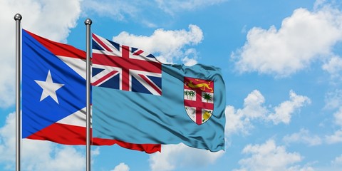 Puerto Rico and Fiji flag waving in the wind against white cloudy blue sky together. Diplomacy concept, international relations.