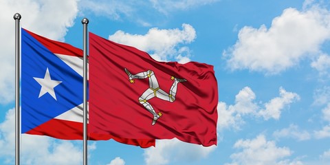 Puerto Rico and Isle Of Man flag waving in the wind against white cloudy blue sky together....