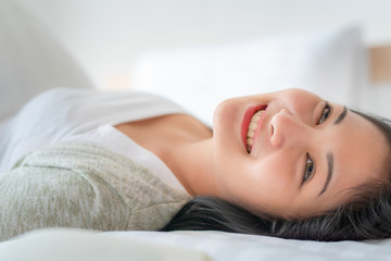 Obraz na płótnie Canvas Beautiful young pretty Asian woman wake up and make happy smile with white shirt at the white bed in the morning.