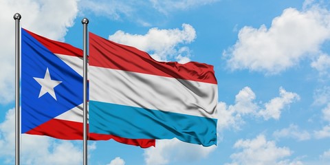 Puerto Rico and Luxembourg flag waving in the wind against white cloudy blue sky together....