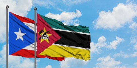 Puerto Rico and Mozambique flag waving in the wind against white cloudy blue sky together....