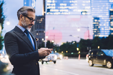 Mature businessman using smartphone against evening New York road