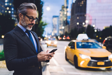 Adult businessman typing on smartphone against evening road