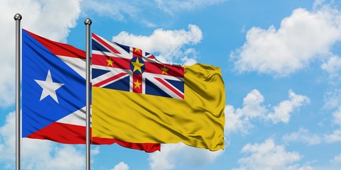 Puerto Rico and Niue flag waving in the wind against white cloudy blue sky together. Diplomacy...