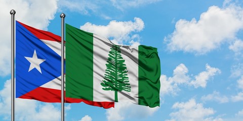Puerto Rico and Norfolk Island flag waving in the wind against white cloudy blue sky together....