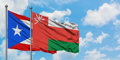 Puerto Rico and Oman flag waving in the wind against white cloudy blue sky together. Diplomacy...