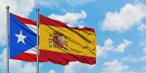 Puerto Rico and Spain flag waving in the wind against white cloudy blue sky together. Diplomacy concept, international relations.