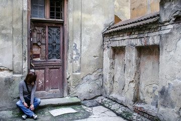 Fototapeta na wymiar A girl in jeans, a striped sweater and sneakers sits on the doorstep by the wooden door of a very old house