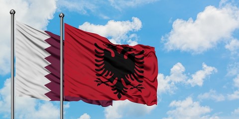 Qatar and Albania flag waving in the wind against white cloudy blue sky together. Diplomacy...