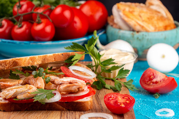 Fototapeta na wymiar Sandwich with chicken meat, cherry tomato and onion on blue background