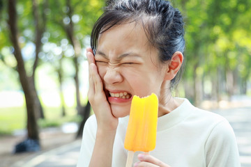 Asian child girl having hypersensitive teeth eating ice-pop,feel painful,female teenage have...