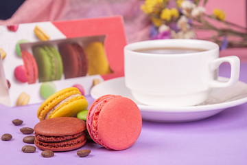 Colorful macarons and cup of coffee, coffee beans over on violet background.
