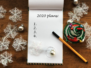 White notebook sheet and pen on wooden table covered with snowflakes, christmas tree and christmas decorations. 2020 plans. New year resolutions. 2020 year