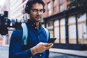 Ethnic young man in earphones using smartphone on street