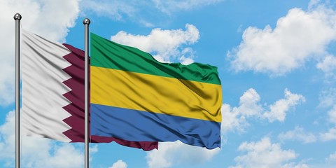 Qatar and Gabon flag waving in the wind against white cloudy blue sky together. Diplomacy concept, international relations.
